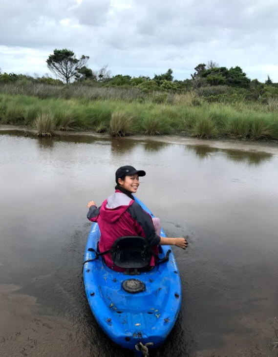 Student collecting water sample in muddy pond